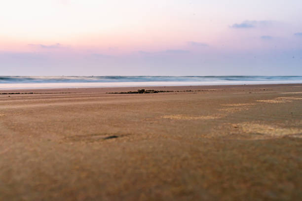 Long exposure, low angle, ground level picture of beach sand in close up with dreamy sea waves and sky in the background. Cavelossim, Goa, India.