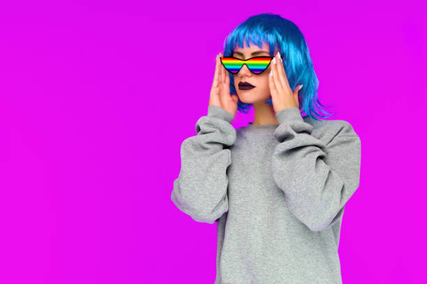 ragazza lesbica con parrucca blu e occhiali da sole arcobaleno guarda di lato su sfondo rosa - girl sunglasses 80s foto e immagini stock