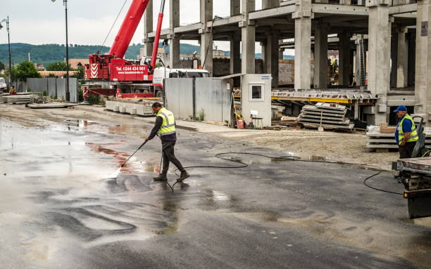 l'ouvrier lave la chaussée sale avec l'eau devant le chantier de construction de centre commercial de festival centrum de la ville de sibiu, roumanie - shopping mall shopping sale retail photos et images de collection