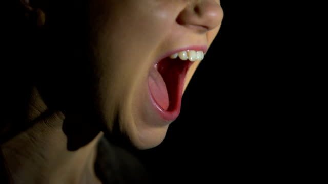 Face of female screaming against dark background, psychological problems