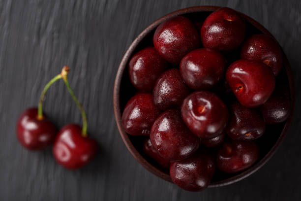 istock Ripe and juicy cherry berries on a black textural background in a brown cup, with water drops. Top view, close-up. 1161753600
