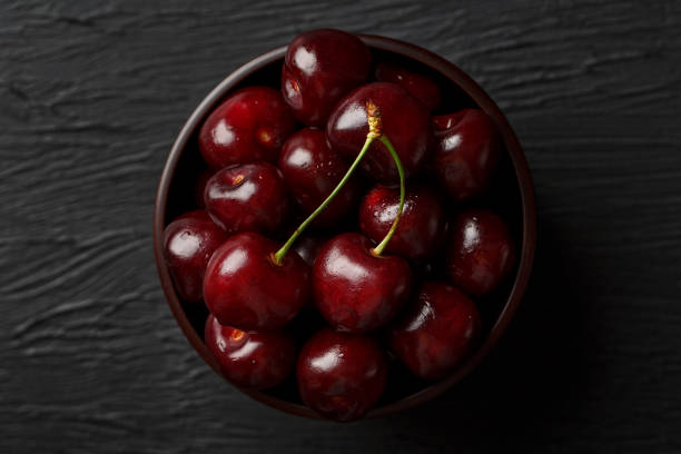 istock Ripe and juicy cherry berries on a black textural background in a brown cup, with water drops. Top view, close-up. 1161753627