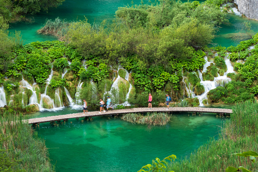 Hikers passing the famous cascades at the Plitvice Lakes National Park. \nPlitvička Jezera, Croatia - June 25th 2019 - Official photography permission obtained by the Plitvice Lakes National Park and available on request.