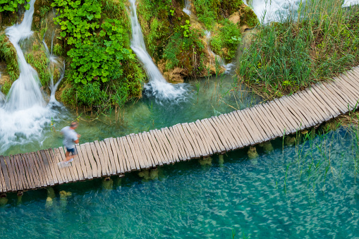 Hiker passing the famous cascades at the Plitvice Lakes National Park. \nPlitvička Jezera, Croatia - June 25th 2019 - Official photography permission obtained by the Plitvice Lakes National Park and available on request.