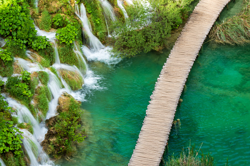 Wooden walkway passing one of the famous natural water cascades at the Plitvice Lakes National Park. \nPlitvička Jezera, Croatia - June 25th 2019 - Official photography permission obtained by the Plitvice Lakes National Park and available on request.
