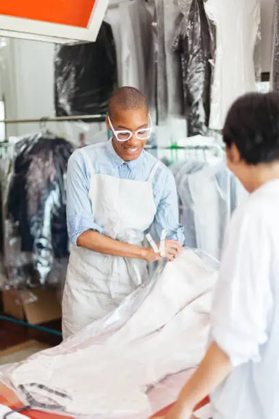 A young woman  is working at a dry cleaning shop and talking to a costumer.