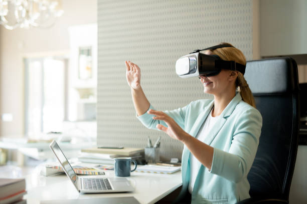Young female employee in vr goggle attenting virtual training Young female employee in vr goggle attenting virtual training while sitting by desk in office virtual reality simulator photos stock pictures, royalty-free photos & images