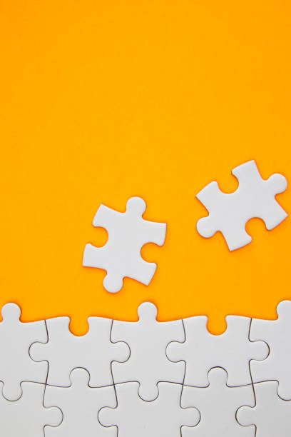 istock White jigsaw puzzle pieces on orange background with negative space 1161780351