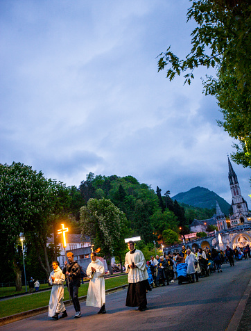 Lourdes, France - May 01, 2019: Evening mess at Sanctuary of Our Lady of Lourdes. People walking and praying holding candles.