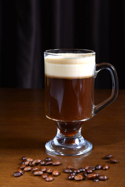 Irish coffee in a glass cup on a wooden table. Dark background. Photo of Irish coffee in a glass cup on a wooden table. Dark background. Nearby are roasted coffee beans. coffee liqueur stock pictures, royalty-free photos & images