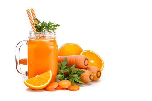 Healthy drink: mason jar filled with fresh organic orange and carrot juice shot on white background. Whole and sliced carrots and oranges are all around the glass. The composition is at the left of an horizontal frame leaving a useful copy space for text and/or logo. Predominant colors are orange and white. High key DSRL studio photo taken with Canon EOS 5D Mk II and Canon EF 100mm f/2.8L Macro IS USM.