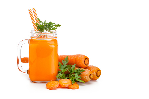 Healthy drink: mason jar filled with fresh organic carrot juice shot on white background. Whole and sliced carrots are all around the glass. The composition is at the left of an horizontal frame leaving a useful copy space for text and/or logo. Predominant colors are orange and white. High key DSRL studio photo taken with Canon EOS 5D Mk II and Canon EF 100mm f/2.8L Macro IS USM.