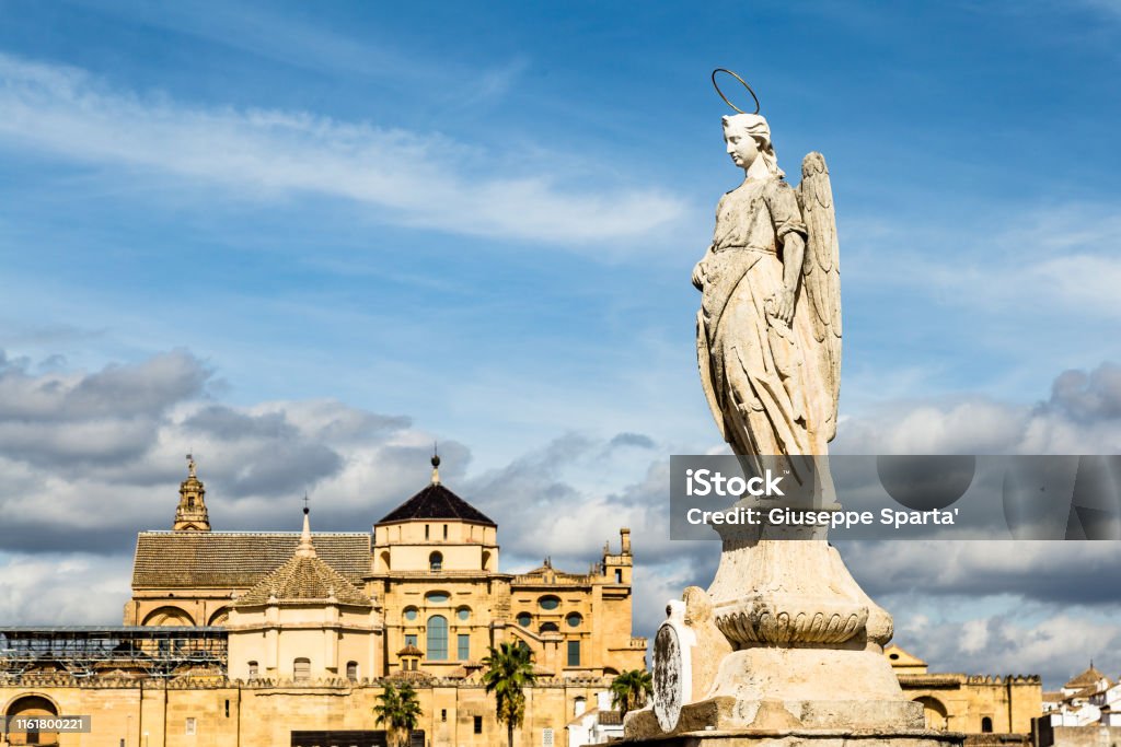 View of Mezquita, Catedral de Cordoba behind an angel statue on the roman bridge. A former Moorish Mosque that is now the Cathedral of Cordoba, Mezquita is a UNESCO World Heritage Site. Ancient Stock Photo