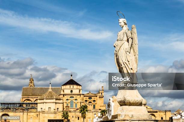 View Of Mezquita Catedral De Cordoba Behind An Angel Statue On The Roman Bridge A Former Moorish Mosque That Is Now The Cathedral Of Cordoba Mezquita Is A Unesco World Heritage Site Stock Photo - Download Image Now