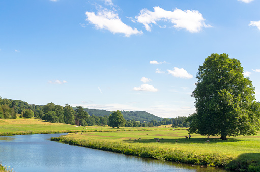 People and livestock by the river as it meanders through the Peak District and Wye Valley countryside in the English summer