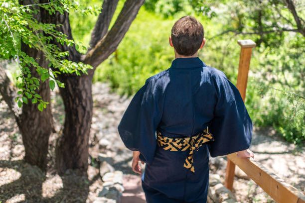 joven con traje de kimono caminando hacia atrás sosteniendo en la valla de barandilla en el jardín al aire libre en japón con vista a la naturaleza hacia abajo - obi sash fotografías e imágenes de stock