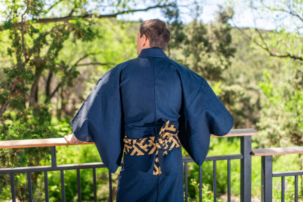 giovane uomo in costume kimono in piedi indietro appoggiato su recinzione ringhiera in giardino all'aperto in giappone con vista sulla natura - obi sash foto e immagini stock