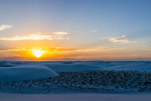 White sands dunes national monument in New Mexico with sun over horizon at sunset with silhouette of Organ Mountains