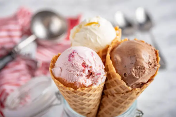 Photo of strawberry, vanilla, chocolate ice cream with waffle cone on marble stone backgrounds