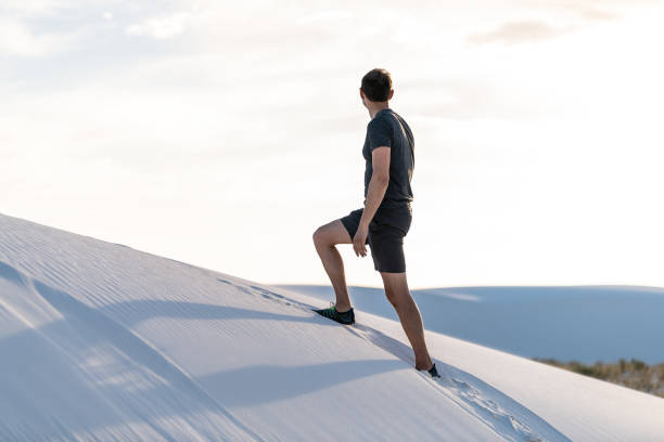 hombre escalando caminando en colina de arena en arenas blancas dunas monumento nacional en nuevo méxico mirando al atardecer - alamogordo fotografías e imágenes de stock