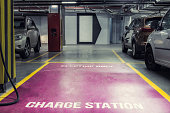 Electric car charging station in underground indoor parking of mall or office building. Reserved parking lot for environment friendly green energy zero emiision vehicles with fast charger plugs