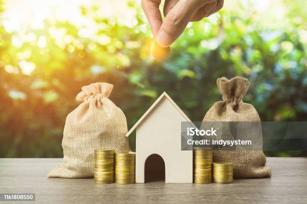Saving Money Home Loan Mortgage A Property Investment For Future Concept A Man Hand Putting Money Coin Over Small Residence House And Money Bag With Nature Background A Sustainable Investment Stock Photo - Download Image Now