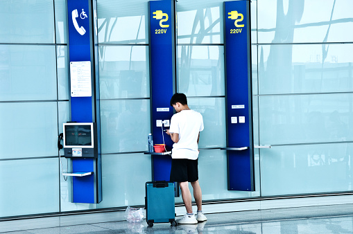 Traveling Chinese passenger using the mobile phone charging station while waiting for his flight in the colourful departure terminal of Beijing Capital International Airport (IATA: PEK, ICAO: ZBAA), Chaoyang–Shunyi, China.