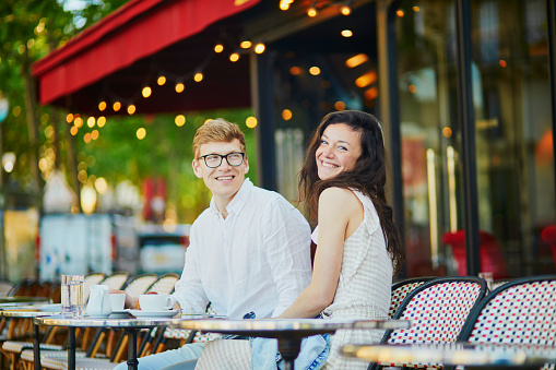 Happy romantic couple in Paris, drinking coffee in traditional Parisian outdoor cafe. Tourists spending their vacation in France