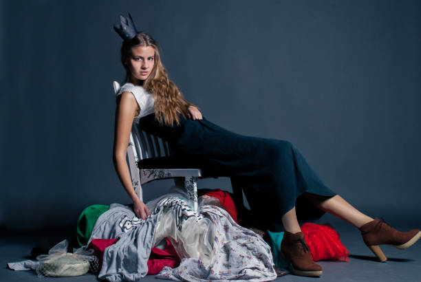 girl in the crown is sitting on a pile of clothes as the queen of consumerism stock photo