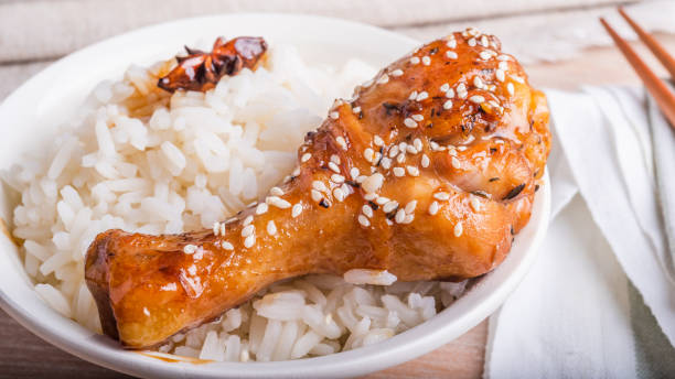 Bowl of rice and chicken drumstick fried in a sticky sweet sauce, sprinkled with sesame seeds, chopsticks, Asian cuisine. Bowl of rice and chicken drumstick fried in a sticky sweet sauce, sprinkled with sesame seeds, chopsticks, Asian cuisine. sticky sesame chicken sauces stock pictures, royalty-free photos & images