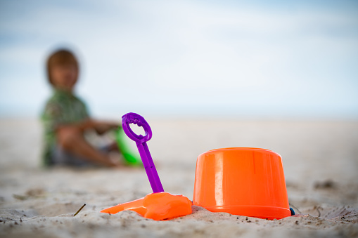 Close up kids toys at the sand beach, boy sitting at the background