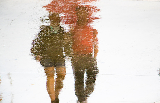 Blurry reflection silhouette in a puddle of couple holding hands while walking on a rainy summer day