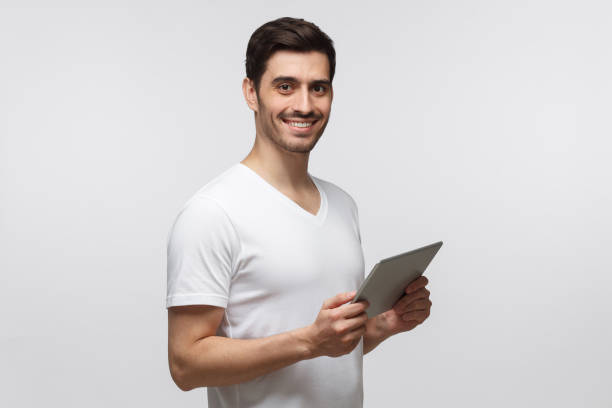 istock Young European man pictured half-turned isolated on background with tablet in hands, looking happily at camera 1161827689