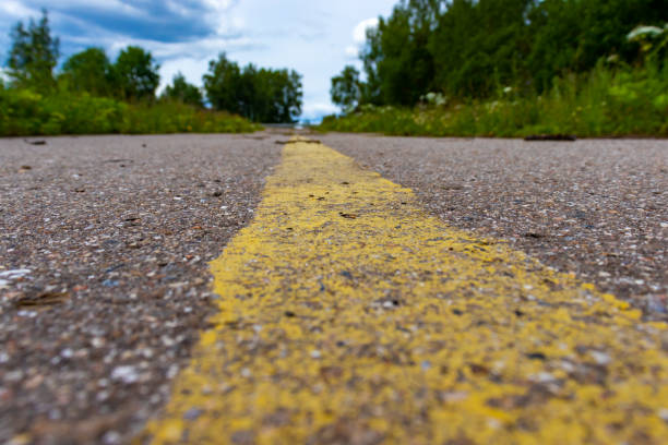 istock Yellow solid line, grunge road marking on asphalt close up with rural landscape on background 1161828006