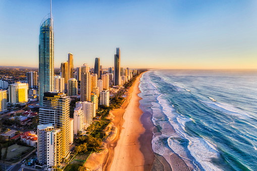 Waterfront behind sandy beach of SUrfers paradise greeting rising sun over Pacific ocean. Aerial view along Gold Coast and line of high-rise towers.
