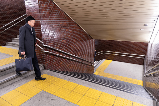 Tokyo, Japan - April 4, 2019: Underground staircase stairs or steps with Japanese businessman with metal railing in Shinjuku train station