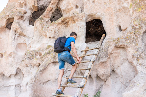 Man climbing ladder on Main Loop trail path in Bandelier National Monument in New Mexico during summer by canyon cliff Man climbing ladder on Main Loop trail path in Bandelier National Monument in New Mexico during summer by canyon cliff los alamos new mexico stock pictures, royalty-free photos & images