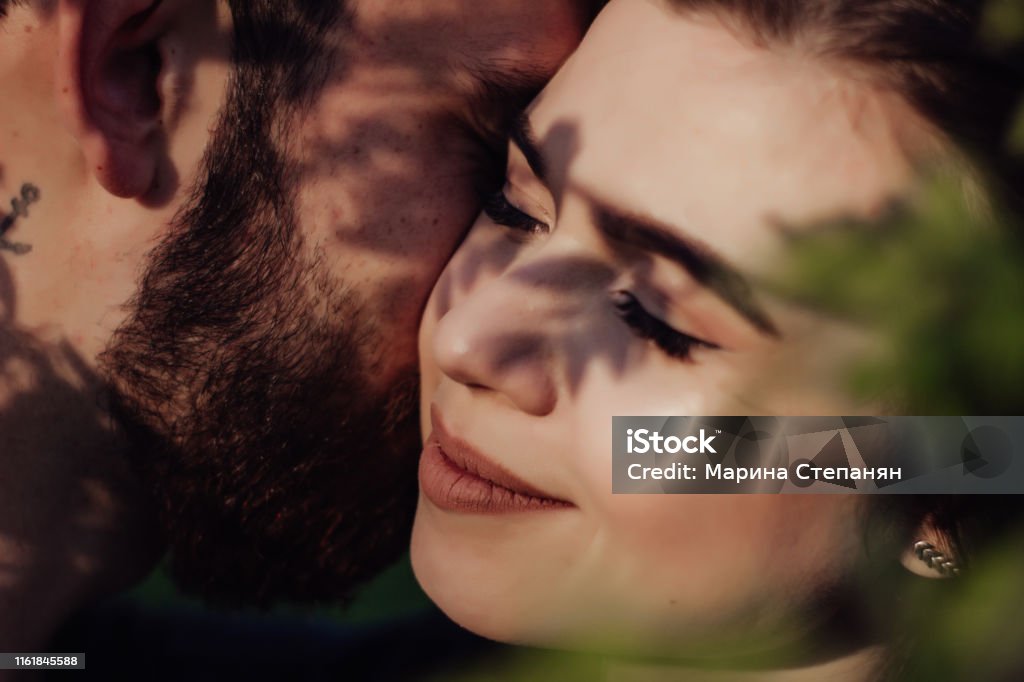 Head shot of young affectionate romantic couple in love. Close up portrait of attractive brunette girl and guy with eyes closed, close to each other. Concept of first kiss, tenderness and amorousness. Art shadow on the face Adult Stock Photo