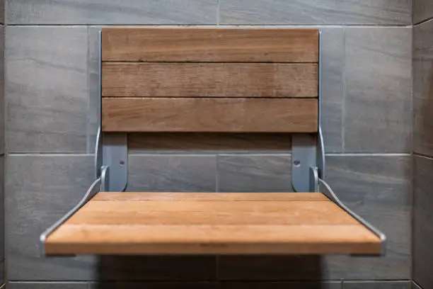 Closeup of staging modern stone grey tiled bathroom in apartment or house with closeup of wooden seat in shower