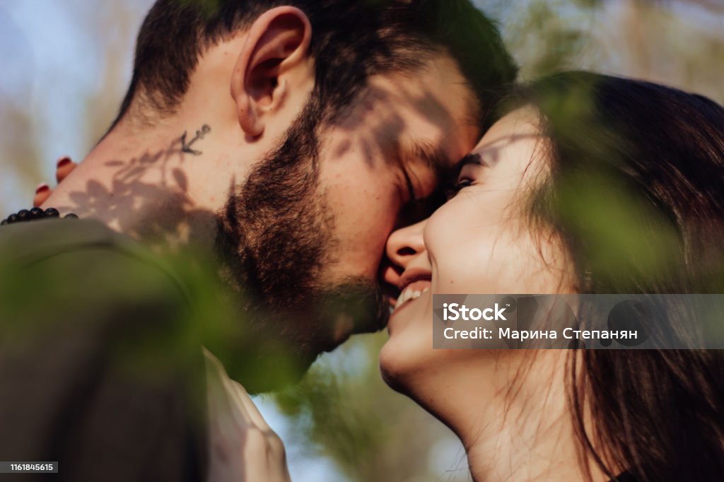 Head shot of young affectionate romantic couple in love. Close up portrait of attractive brunette girl and guy with eyes closed, close to each other. Concept of first kiss, tenderness and amorousness. Art shadow on the face Couple - Relationship Stock Photo