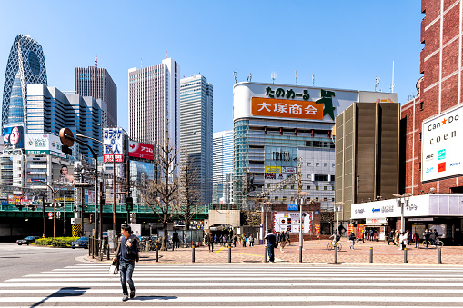 Tokyo, Japan - April 4, 2019: Cityscape or skyline with skyscrapers and cocoon building in Shinjuku near train station, people crossing crosswalk by shopping mall