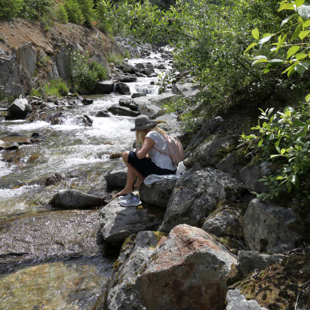 istock Woman with backpack sits on a rock and soaks her feet in a mountain stream 1161861276