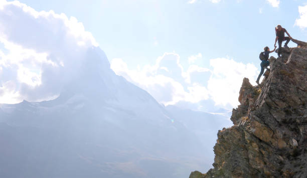 Hikers scramble up steep hillside near the Matterhorn peak They are in profile against the mountains and clouds guidance support stock pictures, royalty-free photos & images