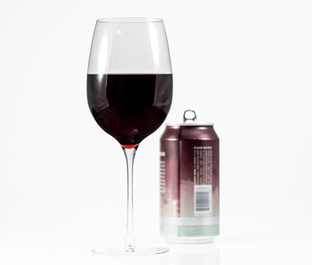 Aluminum can of California Pinot Noir behind a full glass of red wine showing move to single serving cans