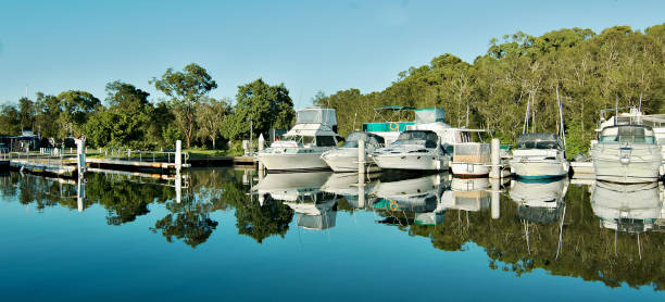 Non-urban waterfront maritime marina/dock with boats. Water reflections at a country marina/dock with boats in tropical water with blue sky backdrop. Bush setting for sailing and cruising vessels. Lake Macquarie, Australia. downunder stock pictures, royalty-free photos & images