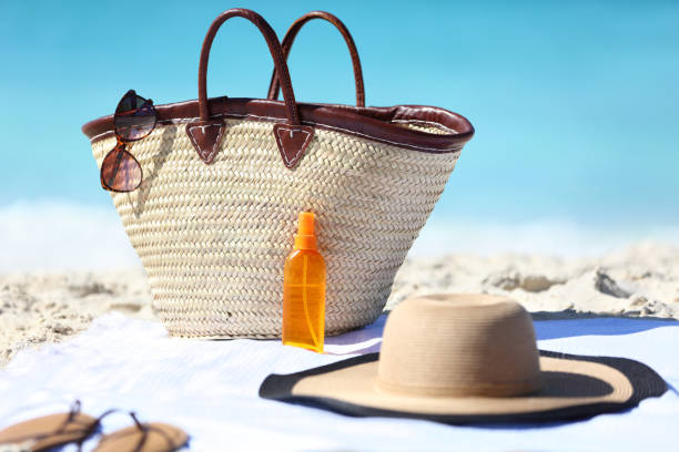 Beach bag and hat, sunglasses and sunscreen lotion Women's beach accessories on sand for summer vacation concept. Straw tote bag, sun hat and sunscreen lotion or suntan tanning oil spray bottle with blue ocean background for travel holidays. beach stuff stock pictures, royalty-free photos & images