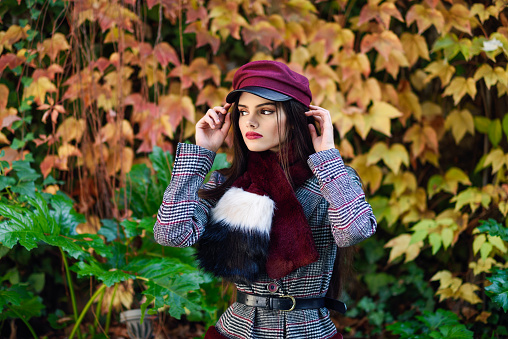 Young beautiful girl with very long hair wearing winter coat and cap in autumn leaves background. Lifestyle and fashion concept.