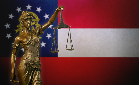 Close-up of a small bronze statuette of Lady Justice before a flag of Georgia.
