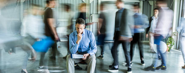 istock Panoramic view of thoughtful businessman reading reports surrounded by his colleagues in blurred motion. 1161926730
