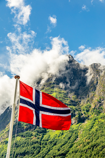Norwegian national flag waving in the wind and mountain's peak in Neroy fjord,  Aurlan, Sogn og Fjordane county, Norway